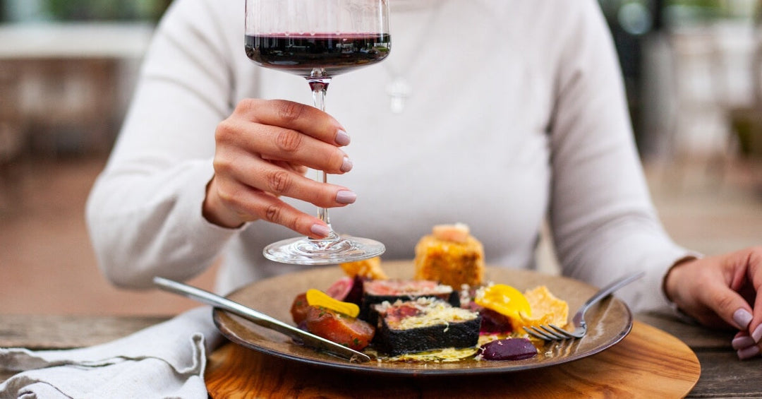 good restaurants in Durbanville feature image - Lady holding a glass of red wine up with a plate of food in front of her